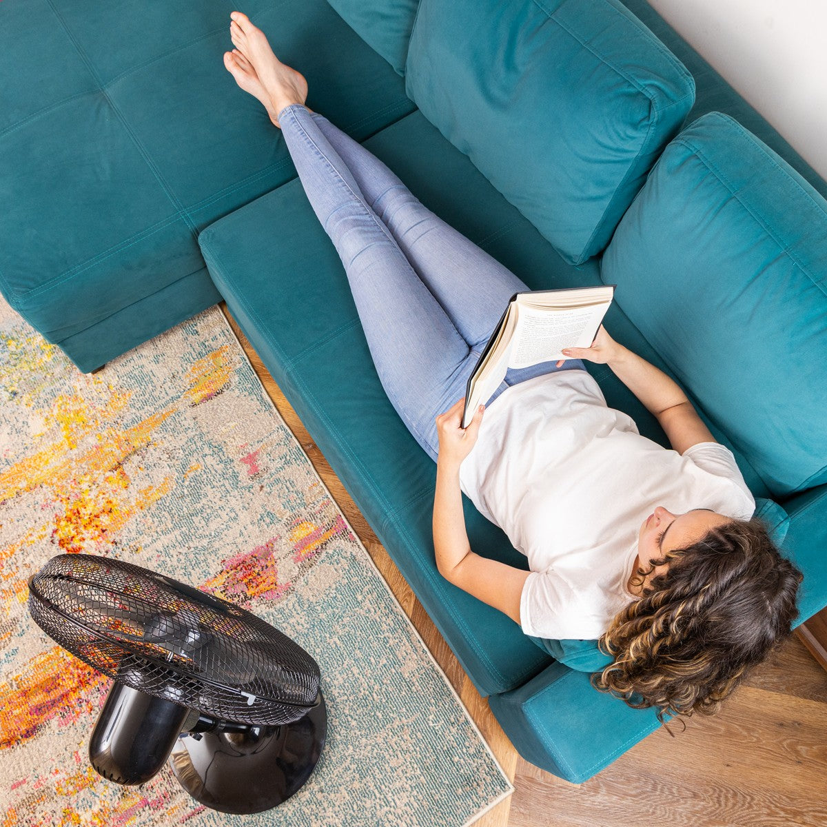 Image of nuovva black cooling pedestal fan (16 inches) cooling woman on the couch - great portable fan. 